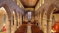 A cathedral interior with stone arches, wooden pews, and stained glass windows.