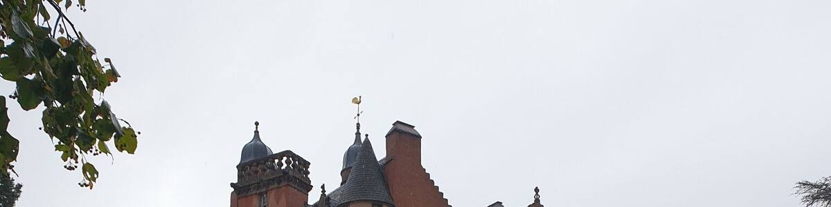 Eine große Burg mit zahlreichen Türmen und Zinnen, umgeben von einer grünen Wiese und Bäumen.