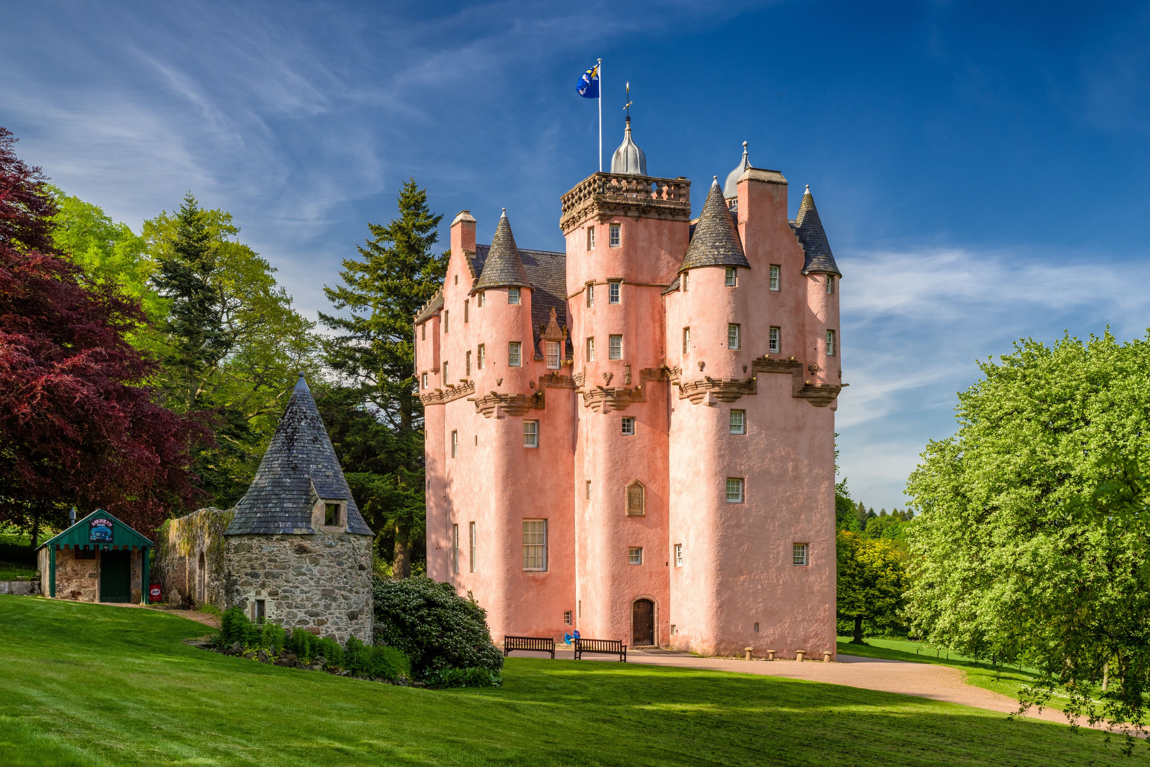 A pink castle with multiple towers, a stone building, and a well-maintained lawn.