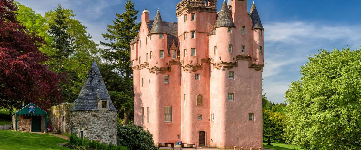 A pink castle with multiple towers, a stone building, and a well-maintained lawn.
