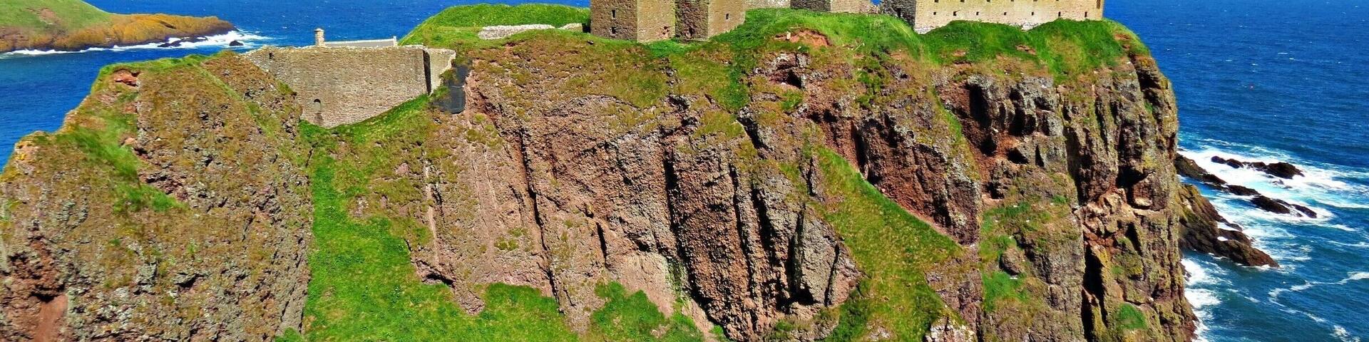 A coastal castle on a rocky cliff with the ocean in the background.