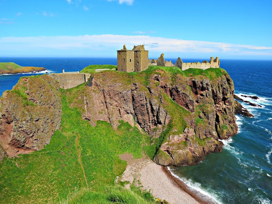 A coastal castle on a rocky cliff with the ocean in the background.