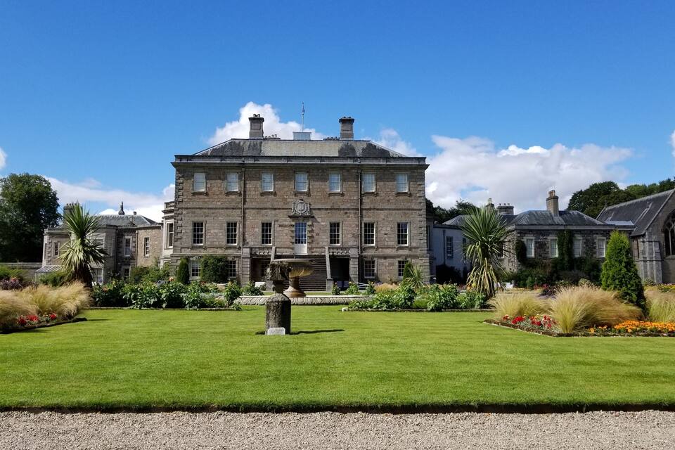 A large stone building with a fountain in the center of a well-manicured lawn.