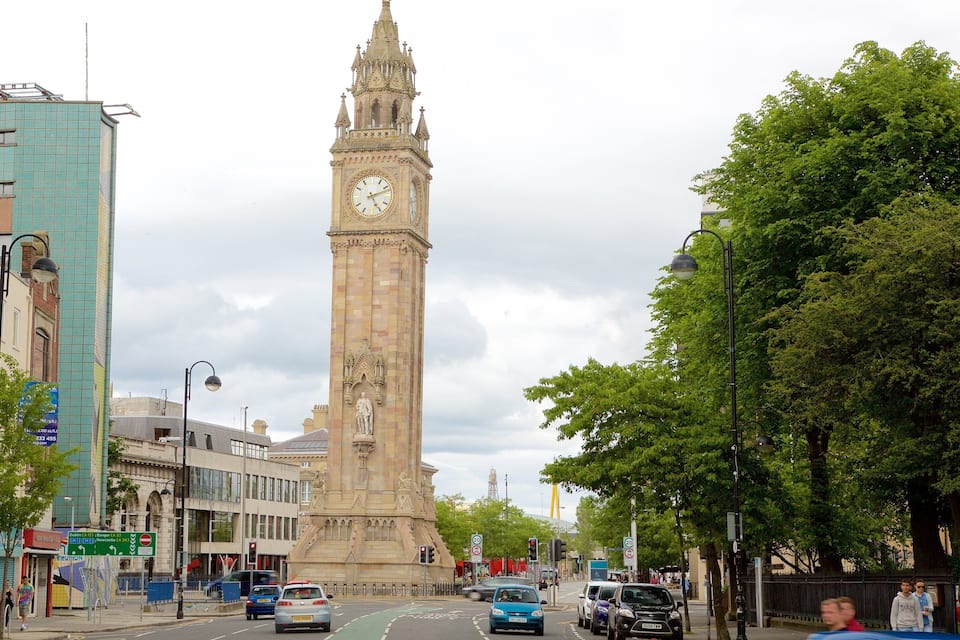 Un'antica torre dell'orologio in una strada cittadina, con edifici moderni e auto.