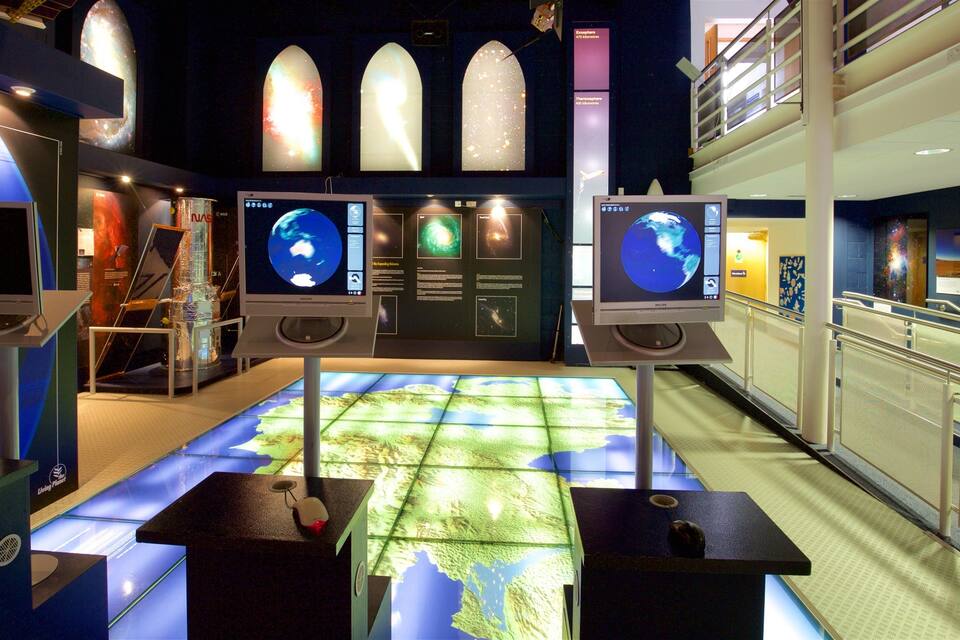 Una exposición de museo con exhibiciones interactivas, que incluye un gran mapa táctil y varias pantallas mostrando imágenes del espacio.