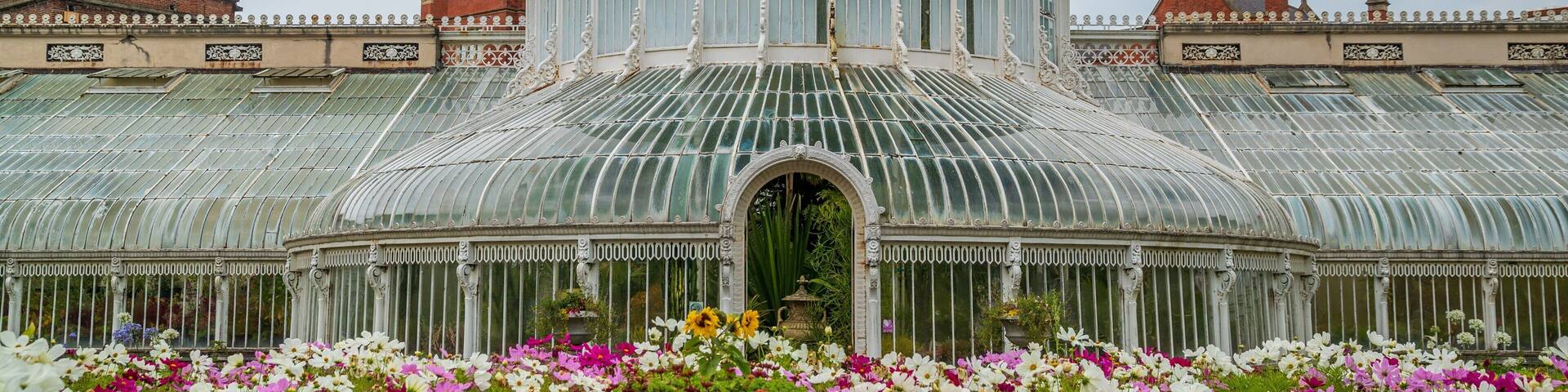 A large glass-domed greenhouse with a metal roof, surrounded by colorful flowers.