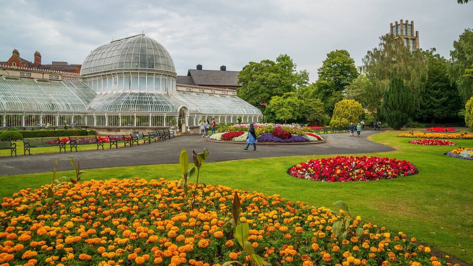 A greenhouse with a glass dome, surrounded by flower beds and benches.