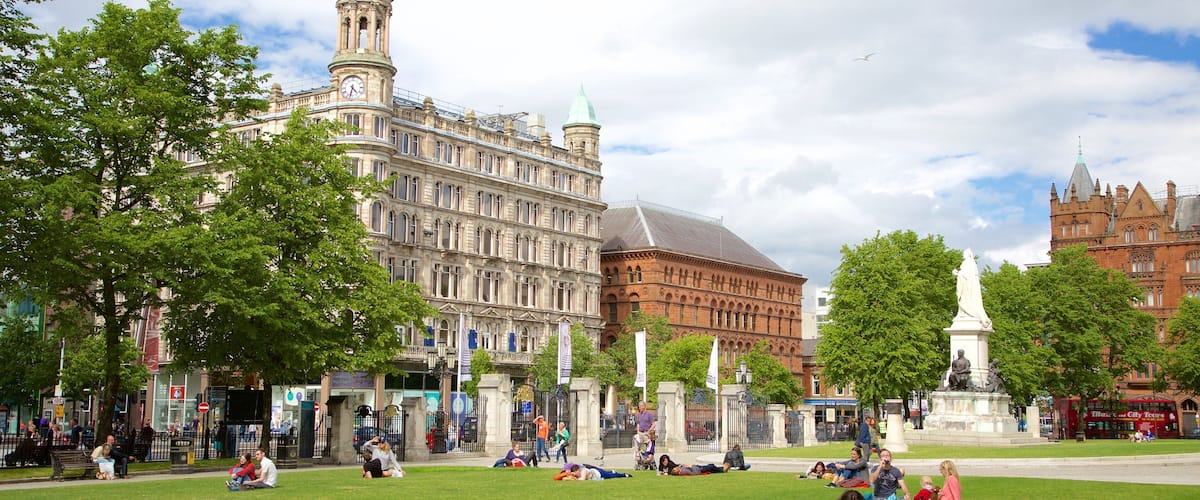 A park with people relaxing on the grass, surrounded by historic buildings and a statue.