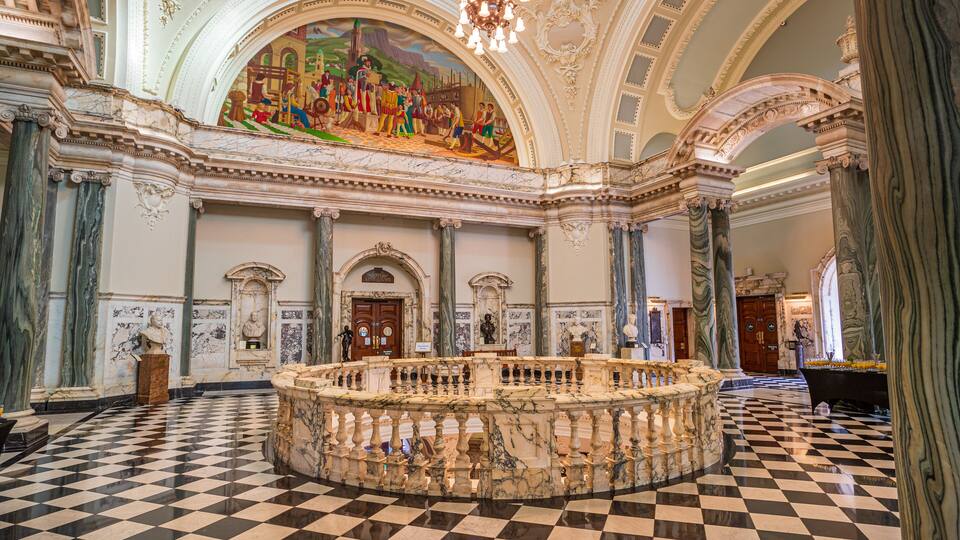 An ornate hall with a checkered floor, marble columns, and a large mural on the ceiling.