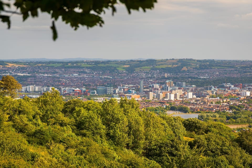 A cityscape with a mix of modern and traditional buildings, surrounded by lush greenery and rolling hills.