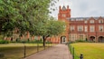 A red brick building with a tower, surrounded by a pathway and greenery.