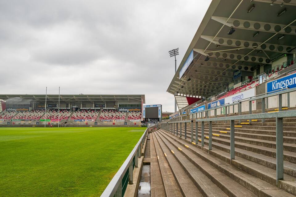 Ein Stadion mit leeren Rängen, einem grünen Spielfeld und Werbung für Kingspan und andere Marken.