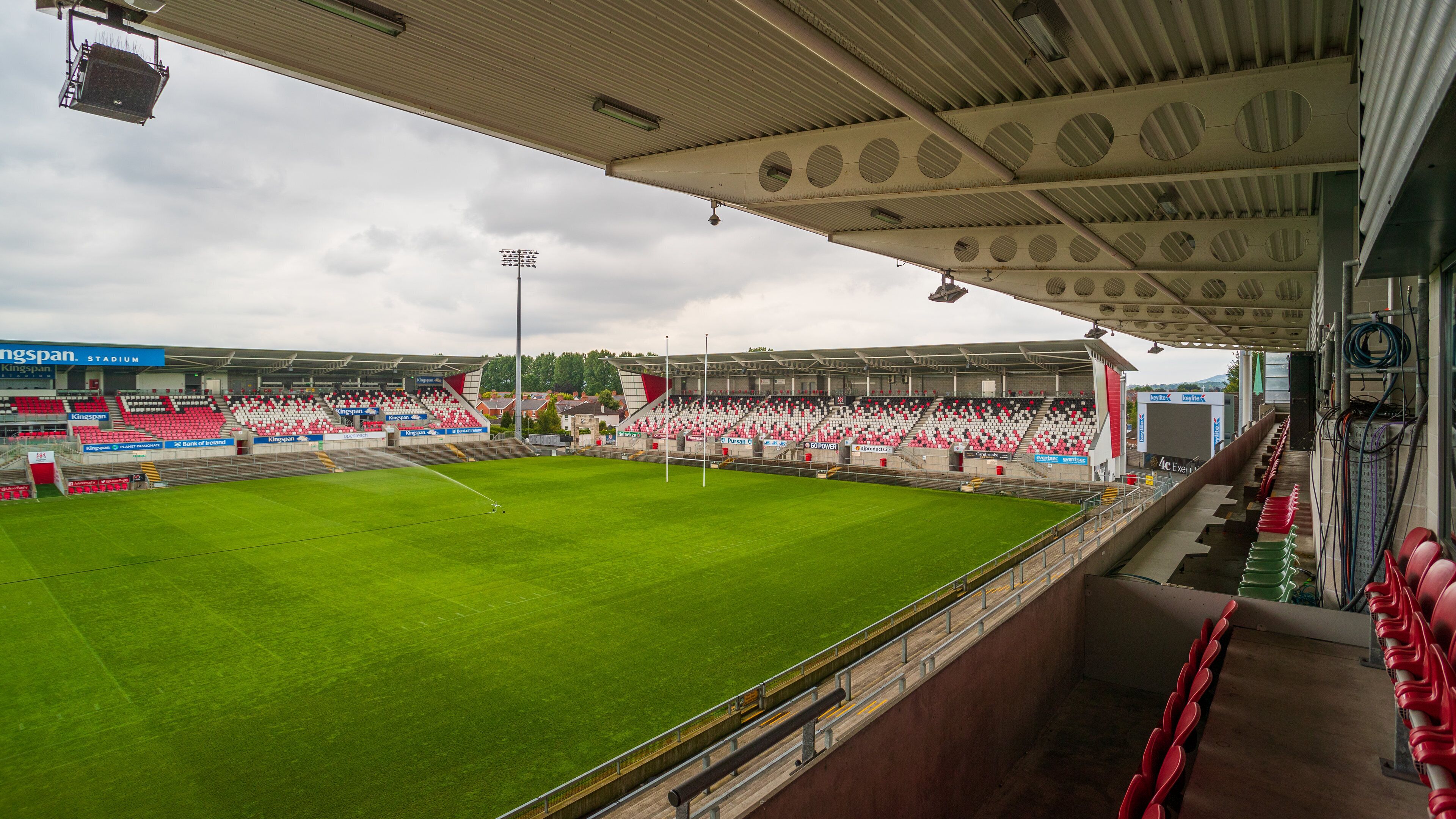 A stadium with a green field, red and white seating, and a covered spectator area.