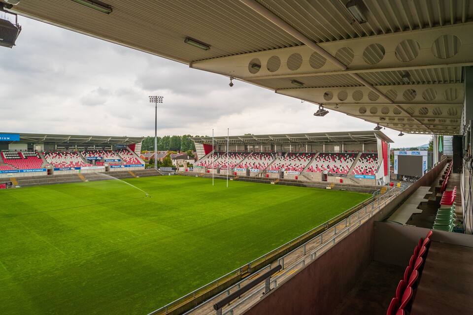 A stadium with a green field, red and white seating, and a covered spectator area.