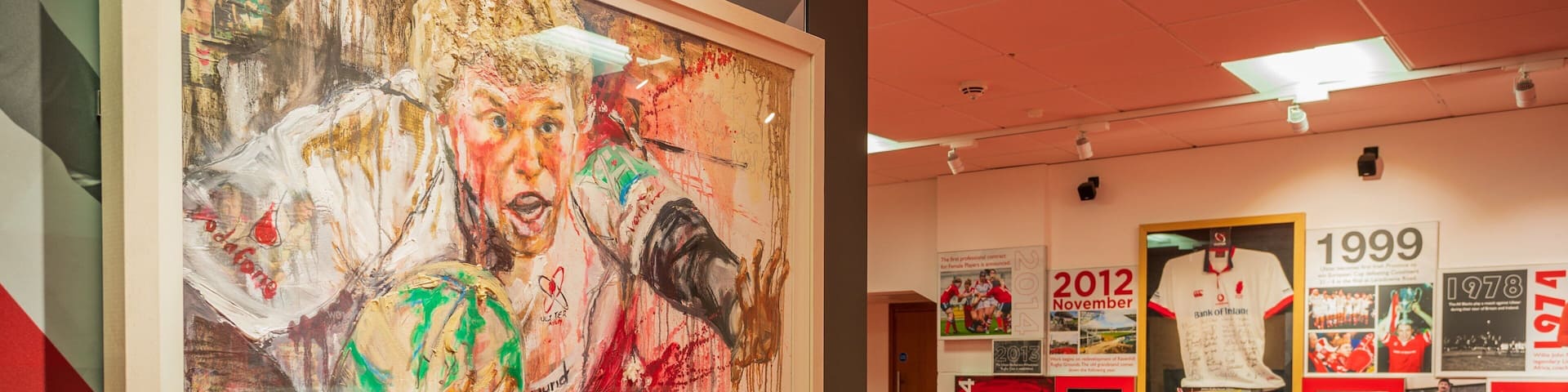 A sports hall with a large abstract painting and memorabilia from 1999 to 2014.