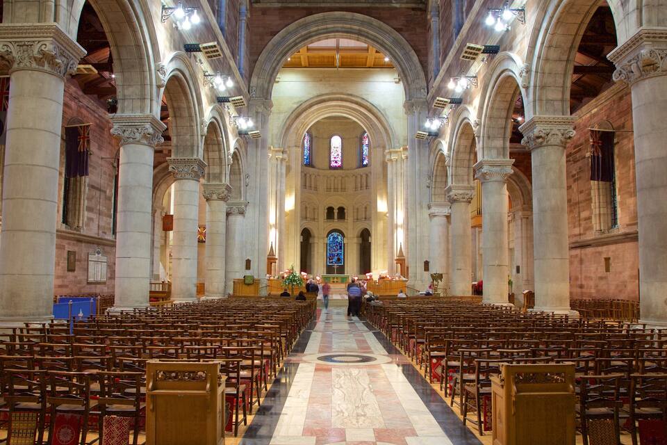 Interno di una chiesa con file di bancali di legno, colonne in pietra e vetrate colorate.