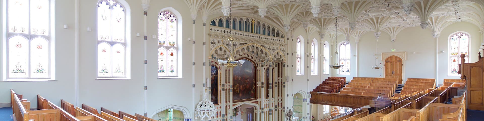 Interior de iglesia con bancos de madera, vidrieras de colores y techo ornamentado.