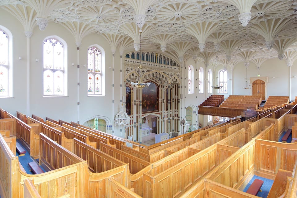 Interno di una chiesa con panche di legno, vetrate colorate e soffitto decorato.