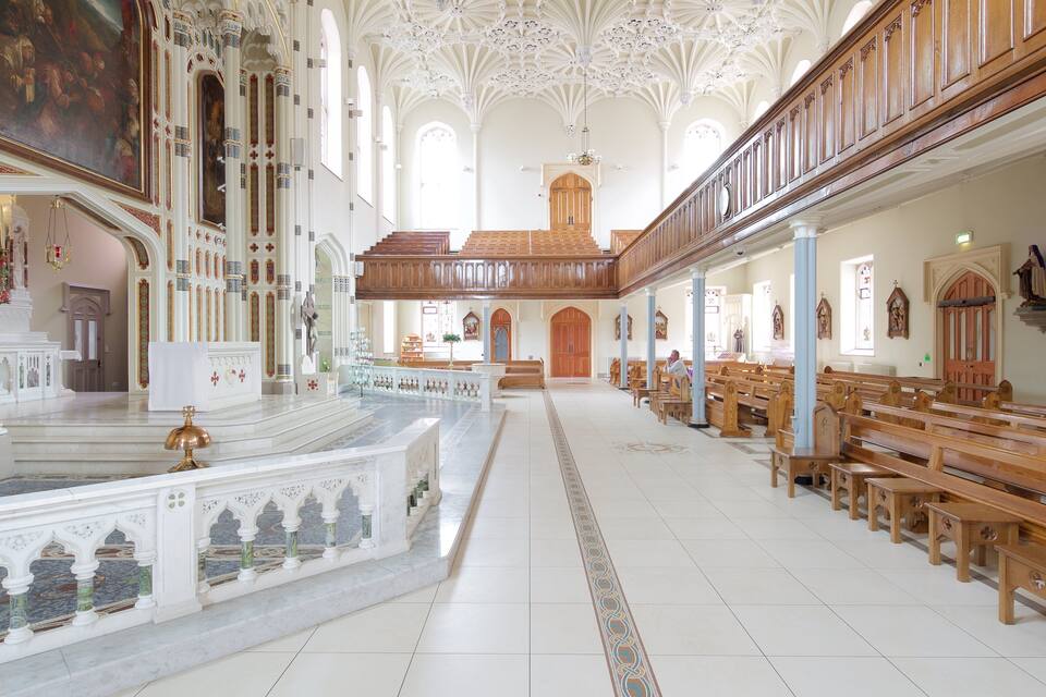 Interior de iglesia con columnas ornamentadas, bancos de madera y un techo alto con diseños intrincados.