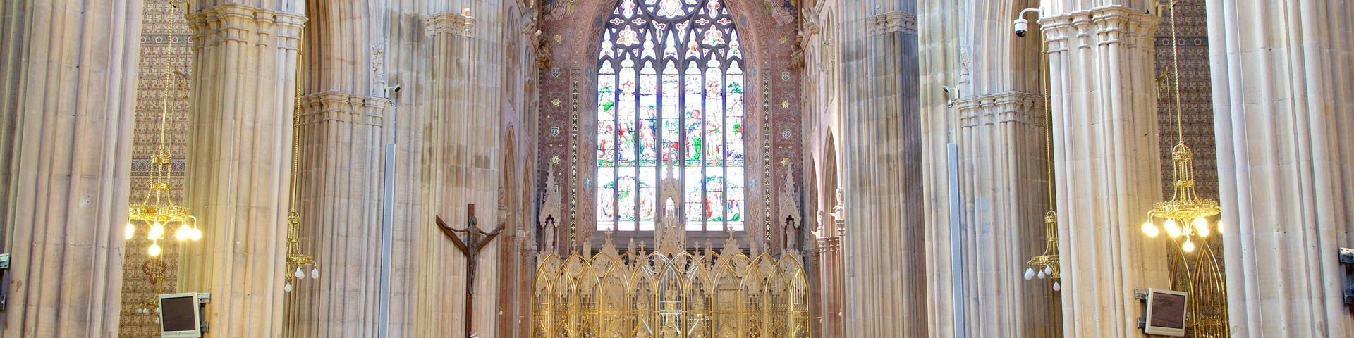 A grand cathedral interior with tall columns, a large stained glass window, and ornate altar.