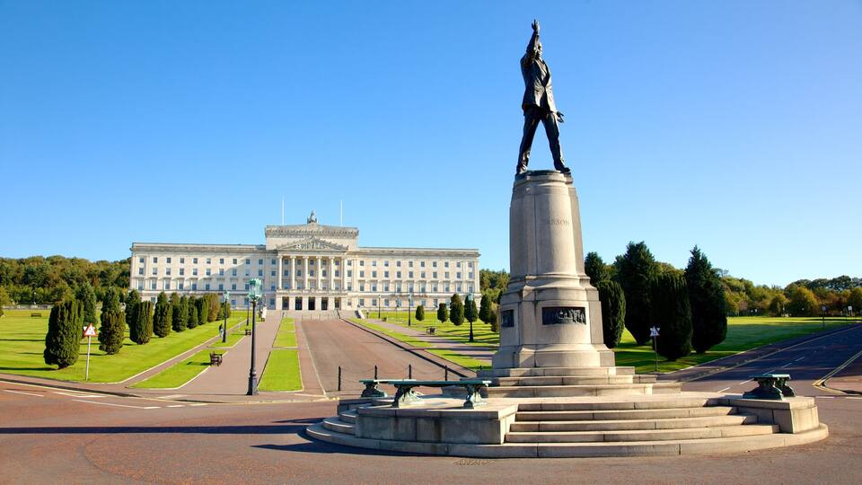 A monument with a statue, a large building in the background, and a well-maintained lawn.