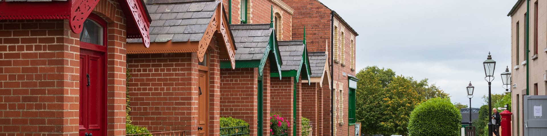 A cobblestone street lined with red brick buildings, green awnings, and a red mailbox.