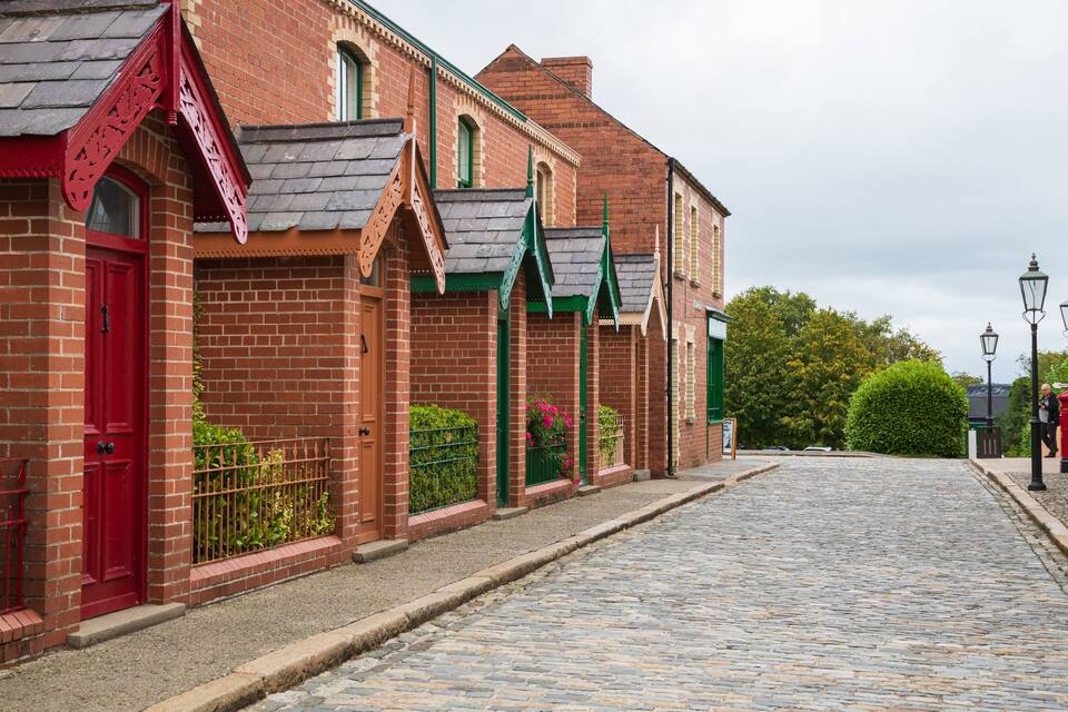 Una calle adoquinada flanqueada por edificios de ladrillo rojo, toldos verdes y un buzón rojo.