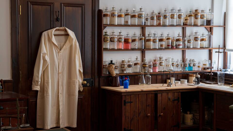 Un laboratorio antiguo con armarios y estanterías de madera llenas de frascos de vidrio etiquetados con nombres de productos químicos.