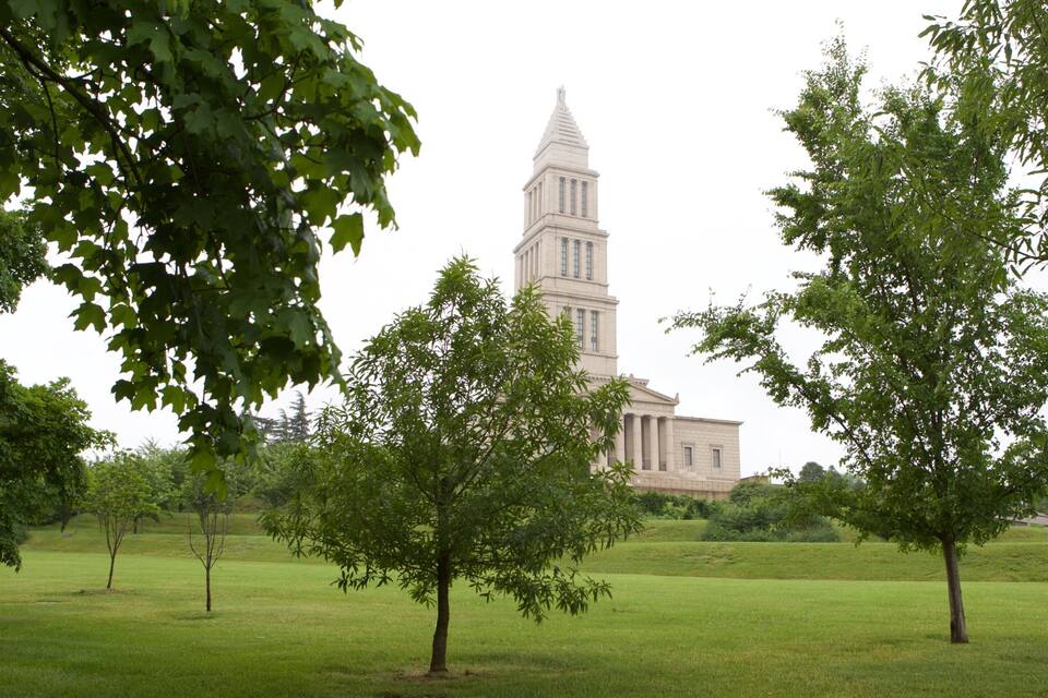 A historic building with a tall tower, surrounded by lush green trees and grass.