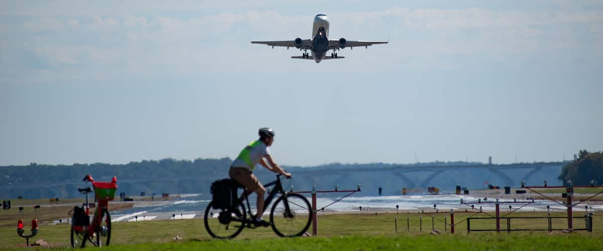 Arlington, Virginia, USA - September 29, 2021: Plane Takes Off from Ronald Reagan Washington National Airport with Bicycle Rider in the Foreground as Seen from Gravelly Point Park