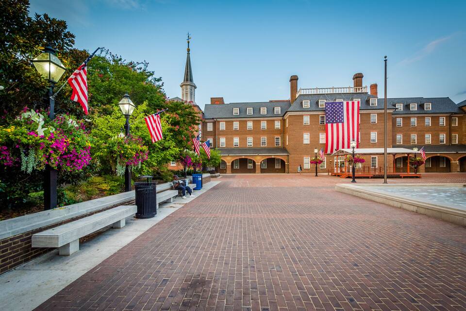 A historic building with American flags, a church spire, and a brick courtyard.