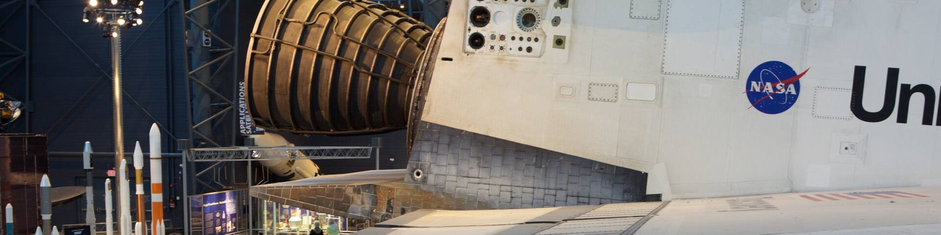 A space shuttle on display at a museum with visitors observing it.