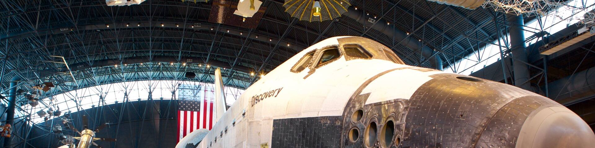 A space shuttle in a museum with a large American flag and the word "Discovery" on its side.