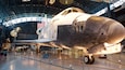 Une navette spatiale exposée dans un musée, avec un grand drapeau américain et le mot « Discovery » inscrit sur son côté.