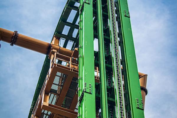 Eine grüne Achterbahnstrecke vor blauem Himmel.
