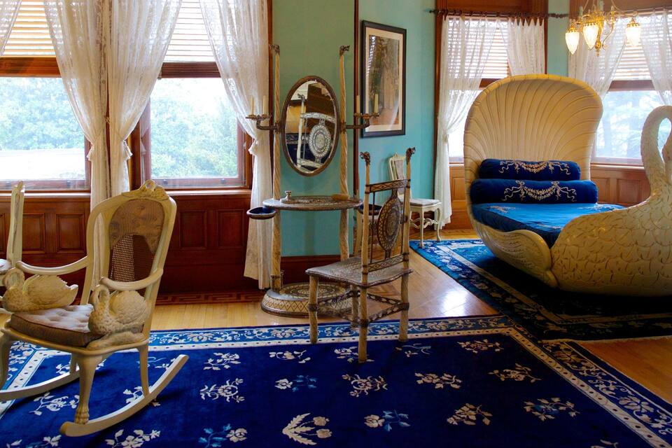 A room with a blue floral carpet, a white swan-shaped chair, a rocking chair, and a wooden side table.