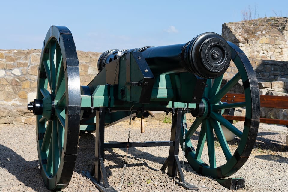 Un cannone storico con ruote verdi e un muro di pietra sullo sfondo.