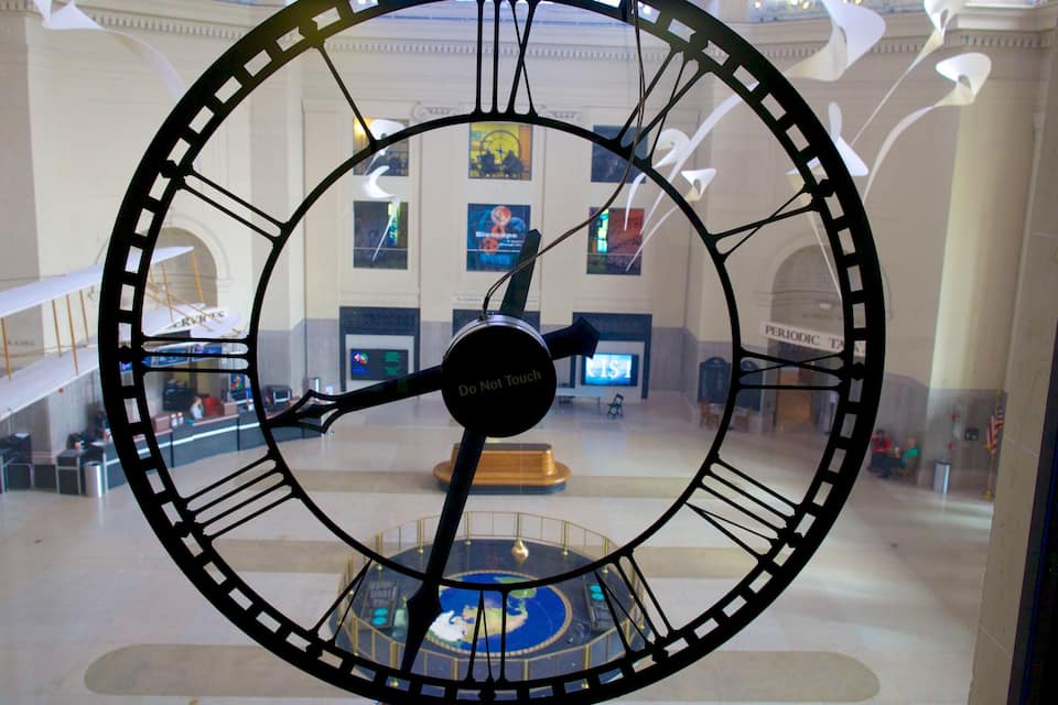 A large clock with a 'Do Not Touch' sign in a public building.