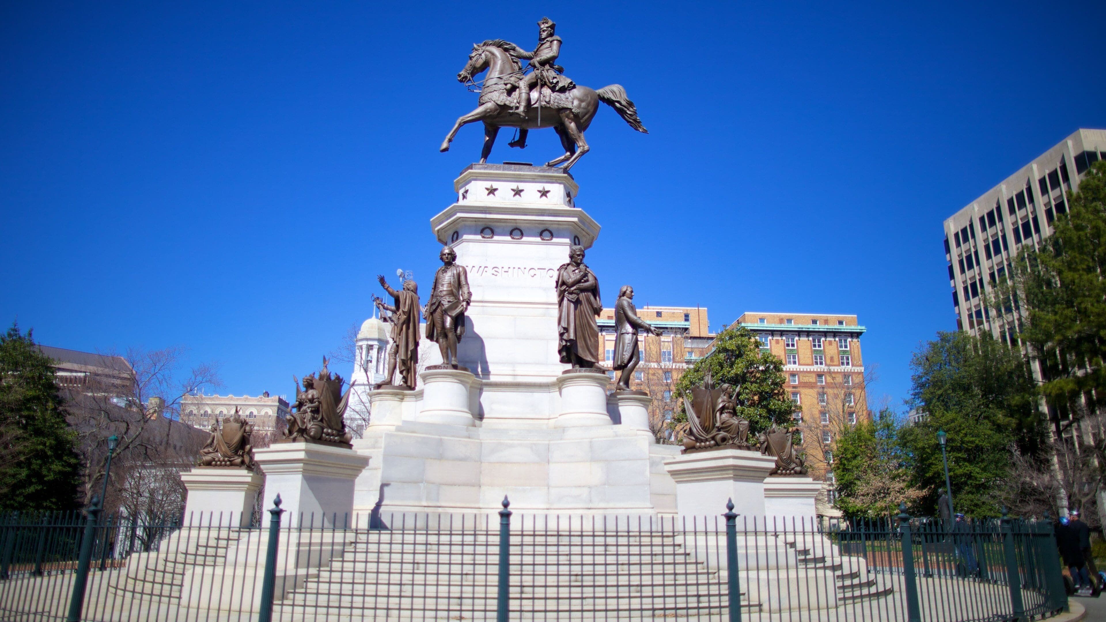 A monument with a central statue of a figure on horseback, surrounded by smaller statues and a fence.