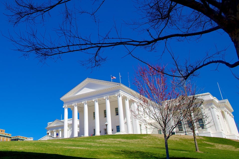 A large white neoclassical building with columns, a flag, and a clear blue sky.