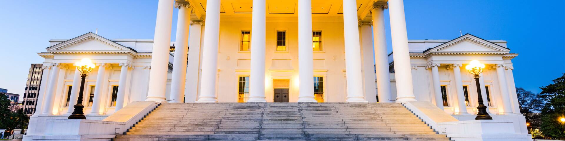A grand neoclassical building with a central portico, large steps leading up to the entrance, and a circular mosaic at the base.