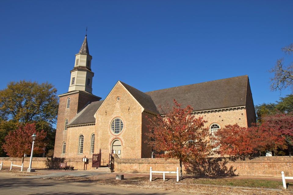 A historic church with a tall steeple and brick walls, surrounded by autumn-colored trees.