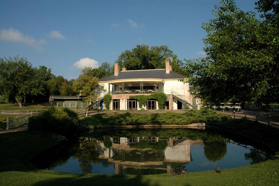A large house with a pond in front, surrounded by trees and a small bridge.