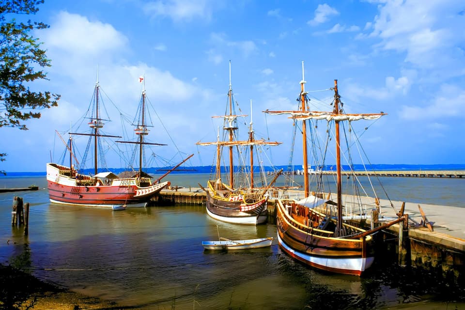 Three large sailing ships docked at a pier with a clear blue sky and calm sea in the background.