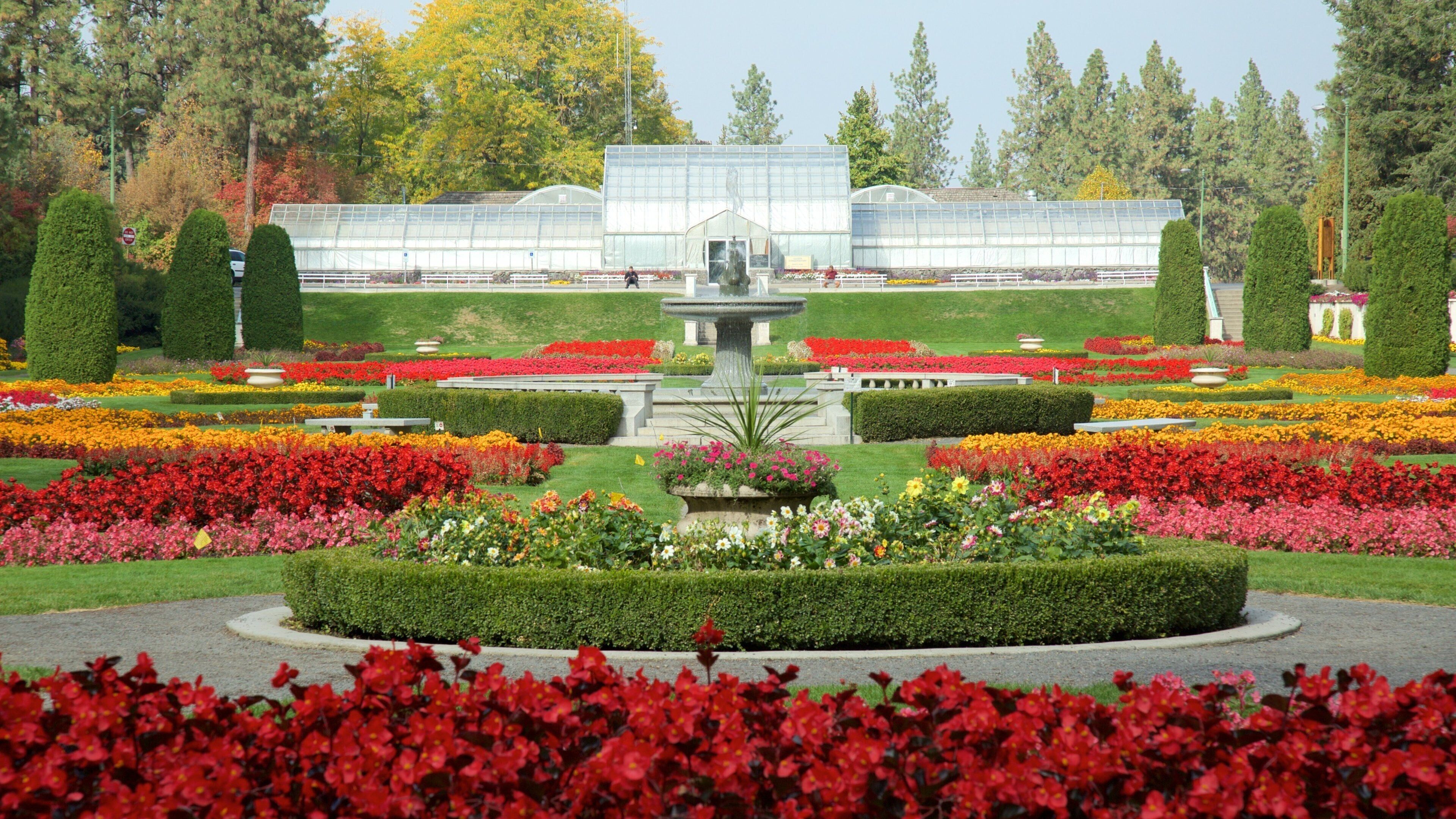 Un jardín formal con una fuente central, setos recortados y coloridos macizos de flores.
