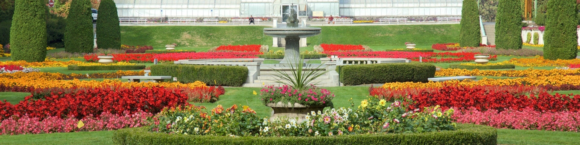 Un jardín formal con una fuente central, setos recortados y coloridos macizos de flores.