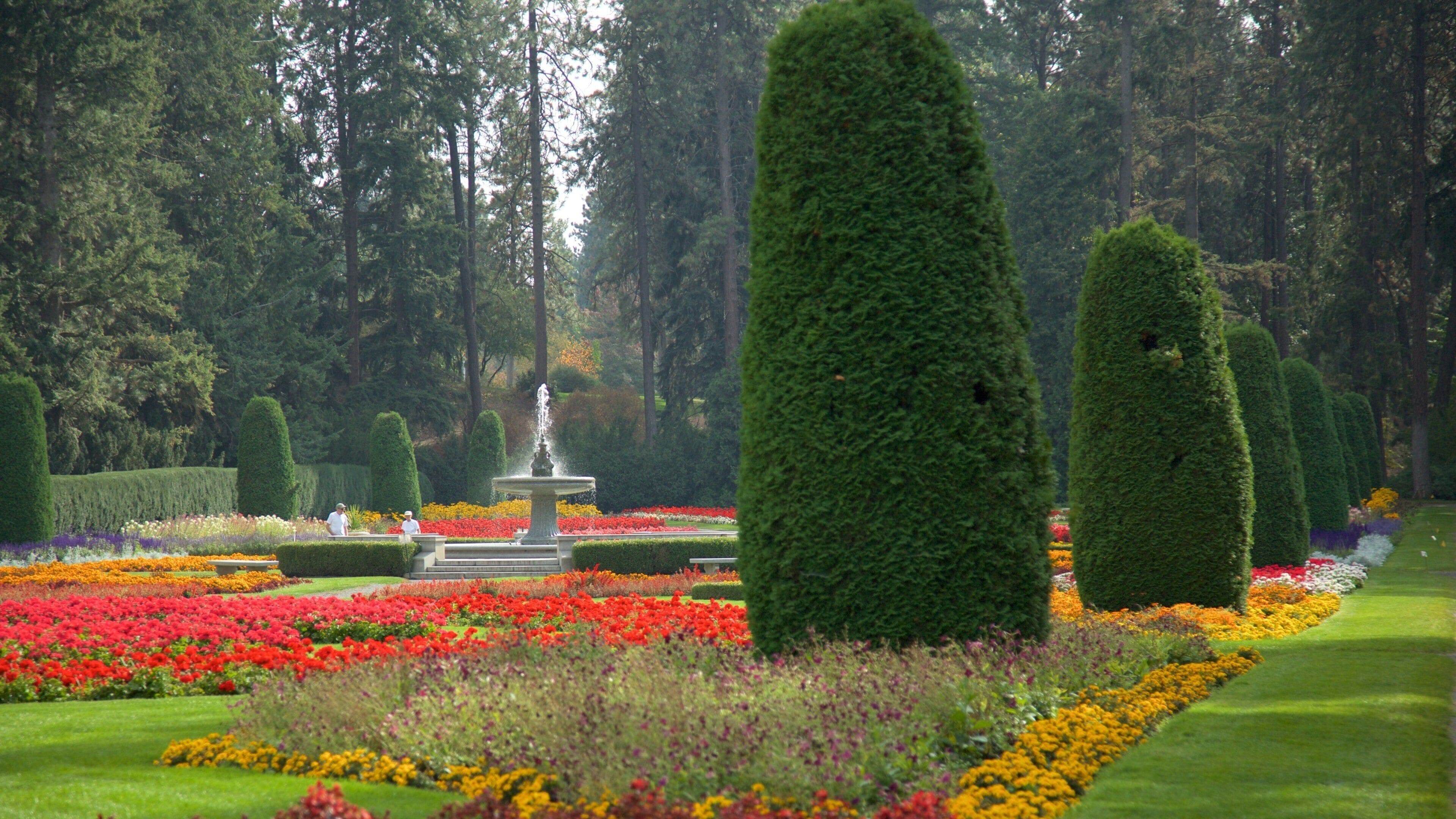 A formal garden with neatly trimmed hedges, a central fountain, and vibrant flower beds.