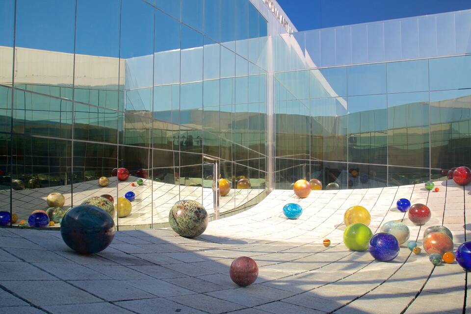 Um edifício moderno com janelas de vidro refletivas e uma praça com esferas de vidro coloridas.