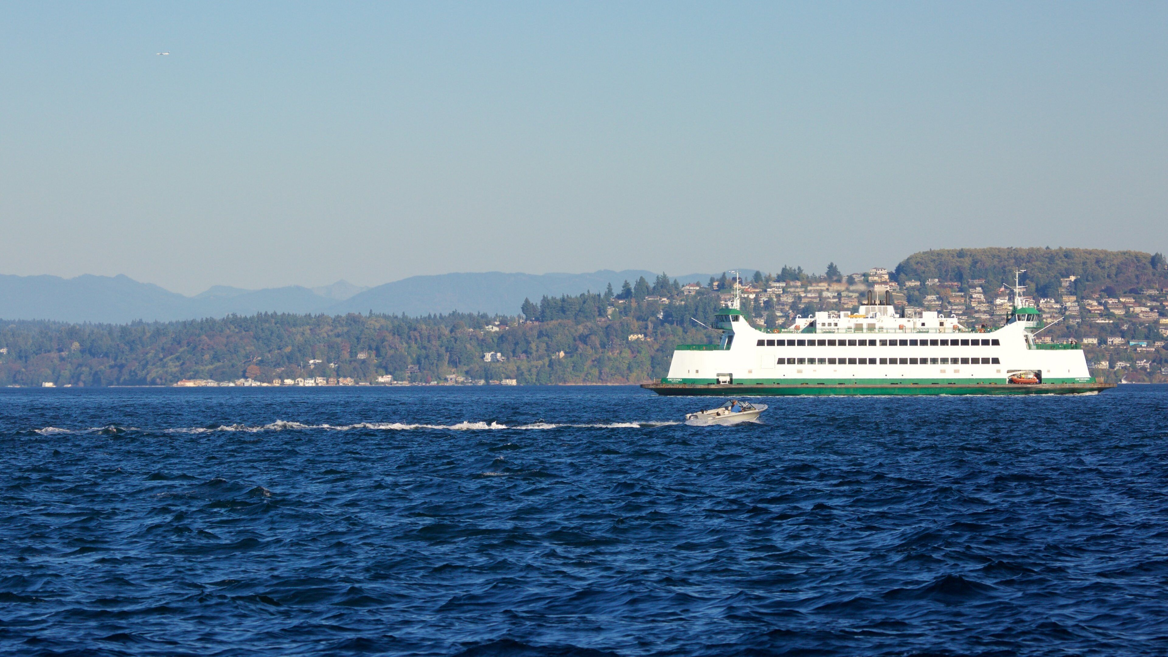 A ferry on a body of water with a mountainous coastline in the background.