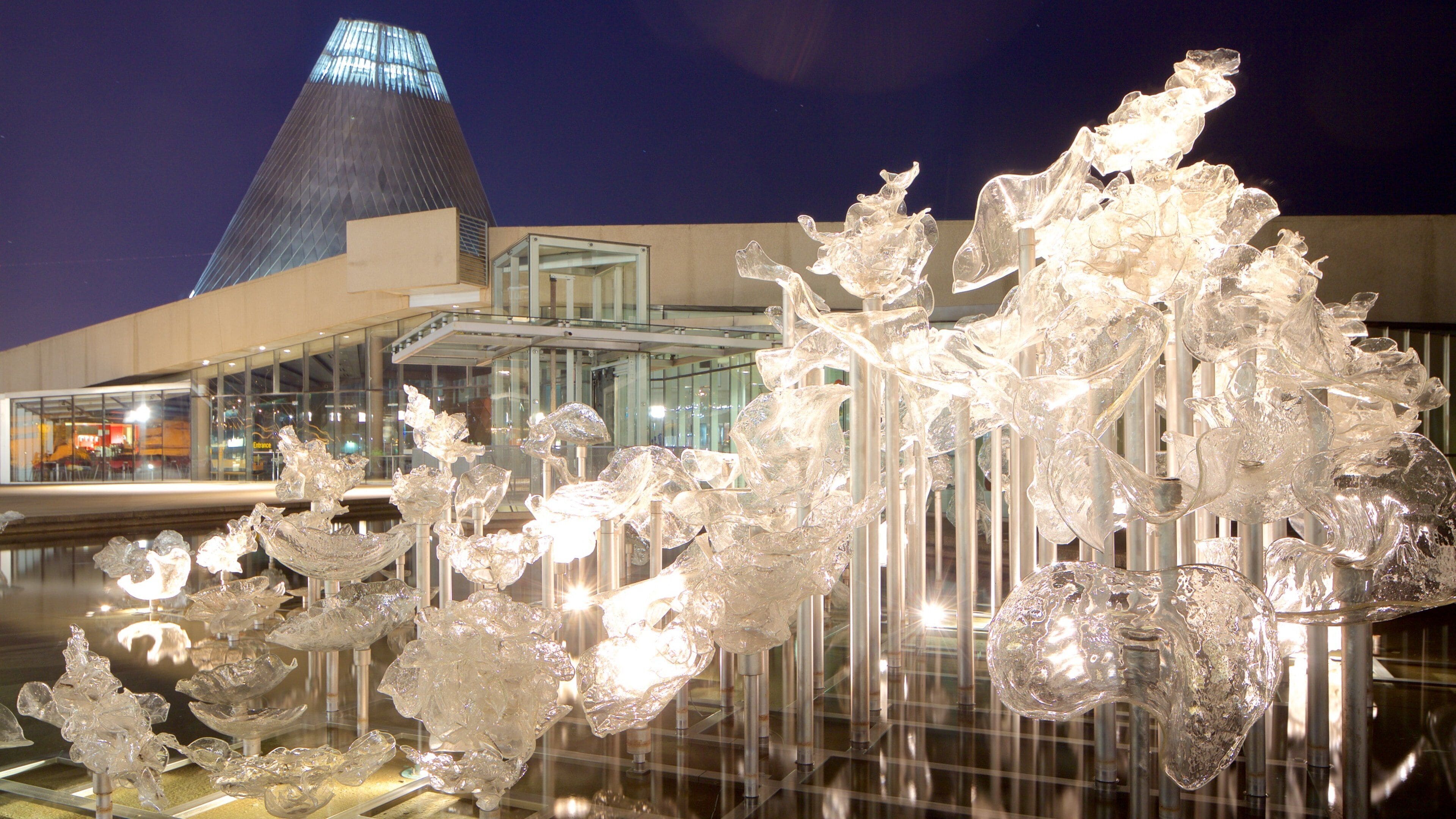 A modern building with a unique glass pyramid structure and a glass sculpture installation in front.